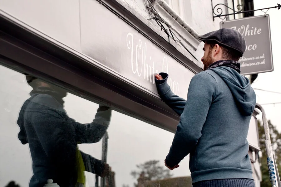 A man working on shop signage in urban area.
